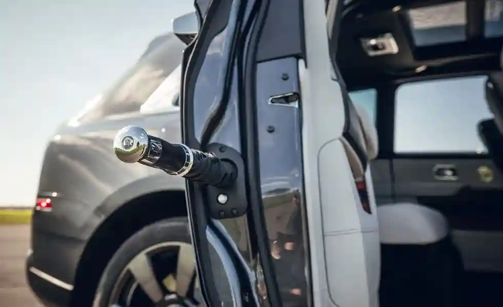 A close-up shot of the iconic Rolls-Royce umbrella with a polished chrome handle, stored inside the custom compartment within the rear door frame of a Cullinan.