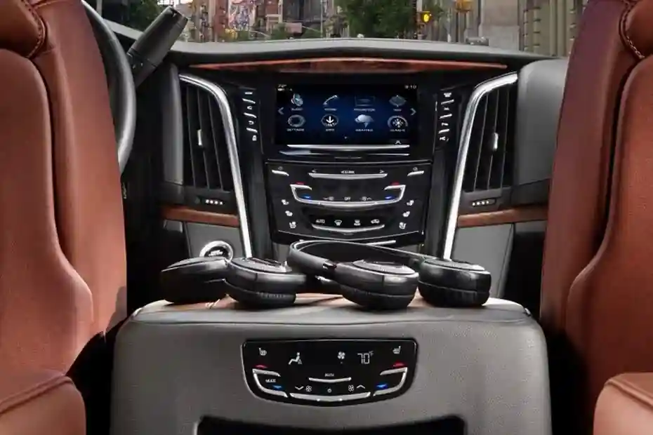 The interior cabin of a luxury SUV featuring tan leather seats, a digital infotainment dashboard, climate control settings, and high-quality wireless headphones resting on the center console for passenger use.