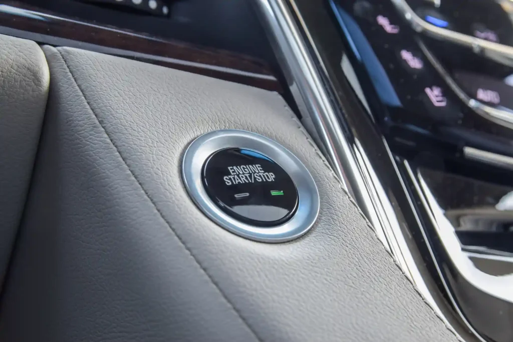 A macro close-up of a silver-rimmed "Engine Start/Stop" button integrated into a light gray stitched leather dashboard of a luxury vehicle, symbolizing modern performance and ease of use.