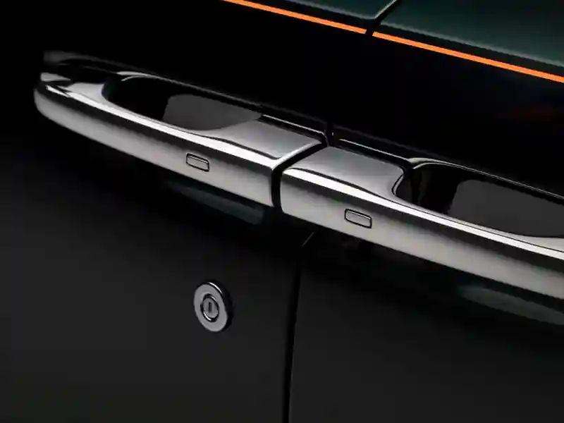 An extreme close-up of the polished chrome door handles on a dark Rolls-Royce, highlighting the iconic rear-hinged coach door design and a vibrant orange coachline running along the body.