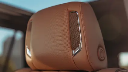 A close-up of a premium tan perforated leather headrest in a luxury vehicle, featuring integrated high-fidelity speakers with chrome accents for a personalized passenger audio experience.
