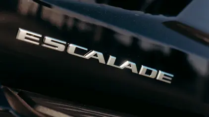 A sharp, close-up shot of the silver chrome "ESCALADE" emblem embossed on the polished black exterior of a luxury SUV, reflecting a clean and prestigious finish.