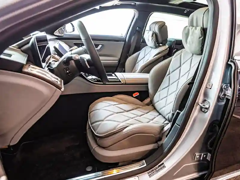 An open-door side view of a Mercedes-Maybach interior featuring diamond-quilted gray leather seats with matching plush headrest pillows and a sleek black dashboard.