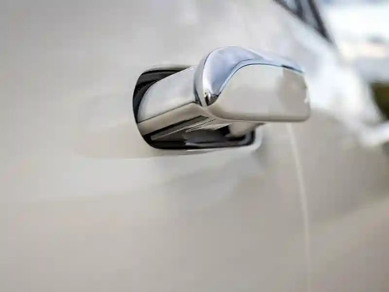 A close-up of a sleek, polished chrome door handle on a white Rolls-Royce, showcasing the seamless integration and high-gloss finish of the vehicle's exterior craftsmanship.