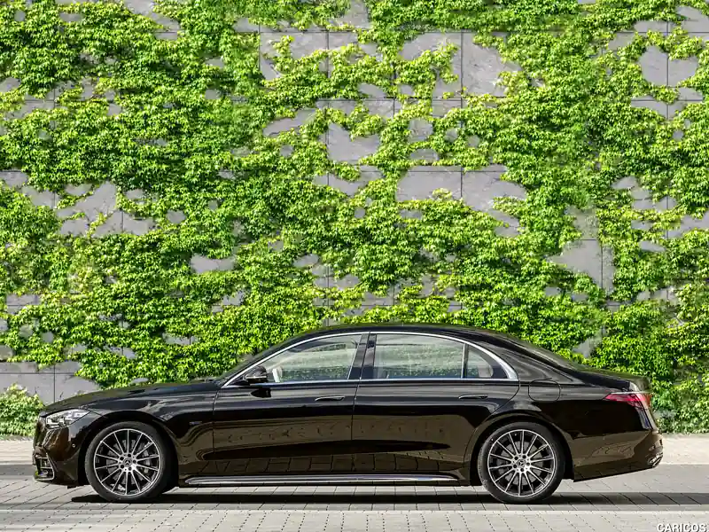 A front-three-quarter view of a black Rolls-Royce Ghost with a subtle gold coachline and blacked-out wheels, parked on a cobblestone courtyard in front of a modern stone building.