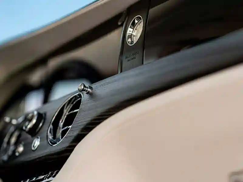 The luxurious rear compartment of a Rolls-Royce, showcasing fold-down wooden picnic tables, plush white leather seating, and premium wood grain door accents.