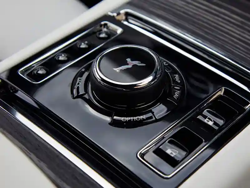 A close-up view of the illuminated Rolls-Royce Ghost dashboard at night, featuring the signature analog clock, glowing white instrument dials, and polished wood veneer under ambient light.