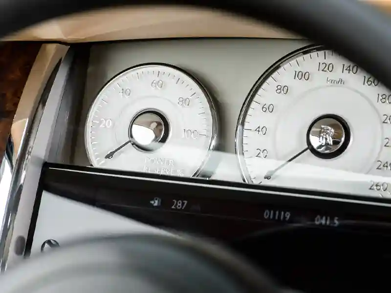 A close-up view of the Rolls-Royce analog instrument panel, showing the elegant white-faced speedometer and the signature Power Reserve gauge with chrome detailing.