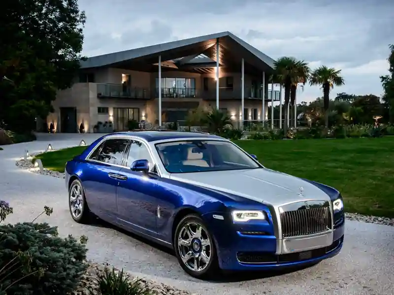 A detailed front view of a Rolls-Royce Black Badge, featuring the darkened chrome Spirit of Ecstasy ornament atop the signature black vertical grille with bright LED daytime running lights.