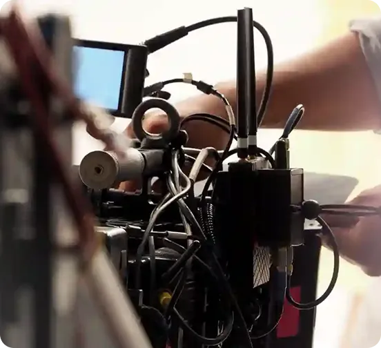 A close-up view of a professional digital cinema camera rig being operated, showing complex wiring, a wireless transmitter with dual antennas, and an external monitor used for high-end film and commercial production.