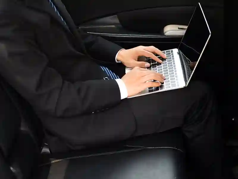 Man with a Laptop inside of the back seat of the Chauffeur Luxury Car