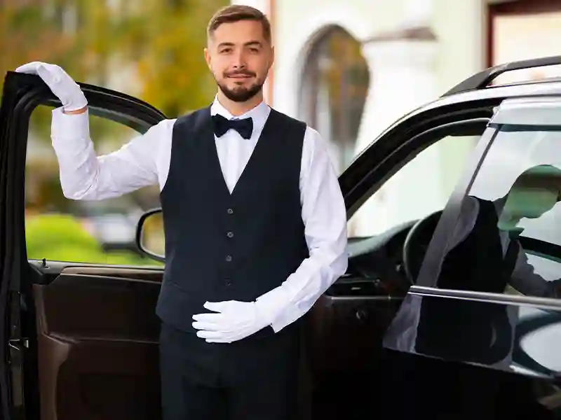 A very well dressed Chauffeur with the front door open, waiting customer