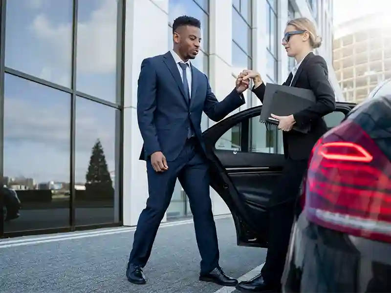 Chauffeur dressed in suit opens the door to an elegant woman coming out the Chauffeur car