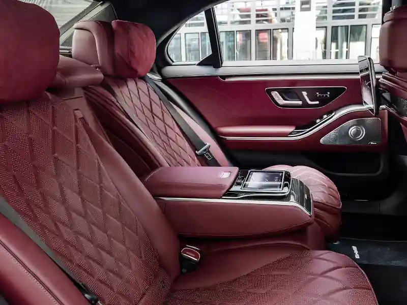 The rear cabin of a luxury Mercedes-Benz S-Class featuring deep red diamond-quilted leather seats, a central control tablet, and premium Burmester speaker grilles, emphasizing a sporty yet sophisticated passenger environment.