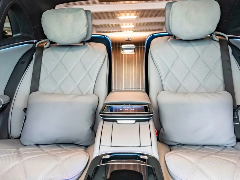 A view of the ultra-luxury rear seating in a Mercedes-Maybach, featuring diamond-quilted gray leather executive seats with plush pillows, pinstriped wood accents, and a central tablet controller for passenger comfort settings.