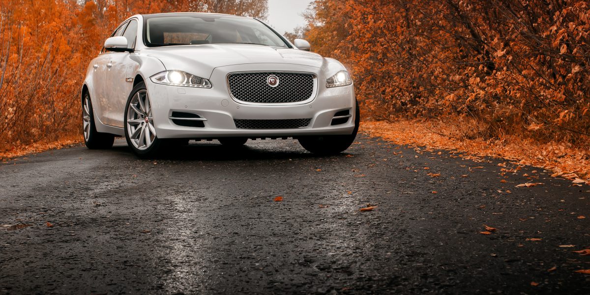 Whtie car Jaguar XJ on wet asphalt road at autumn